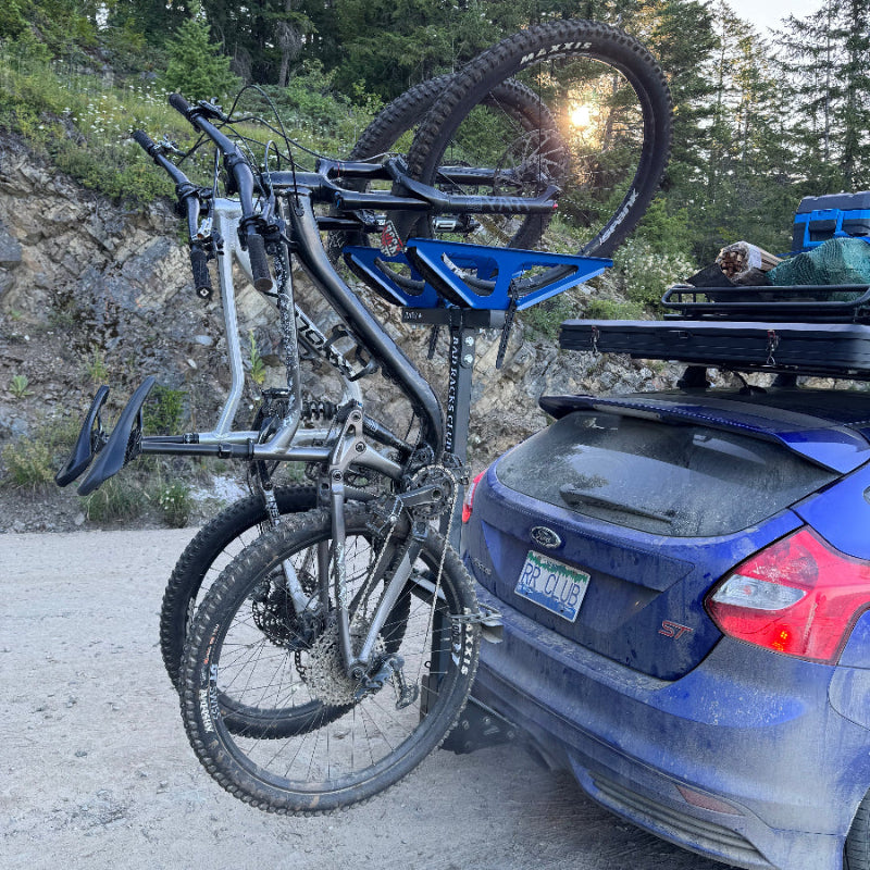Bicycle attached to a car on a road with trees in the background
