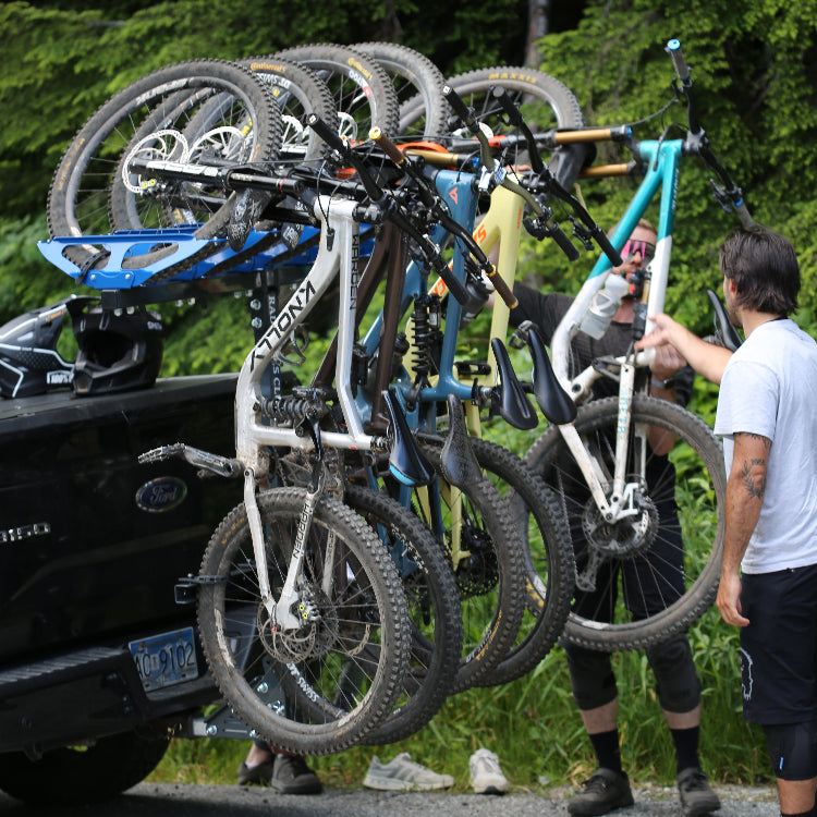 Multiple bicycles on a car roof rack with people adjusting them outdoors.