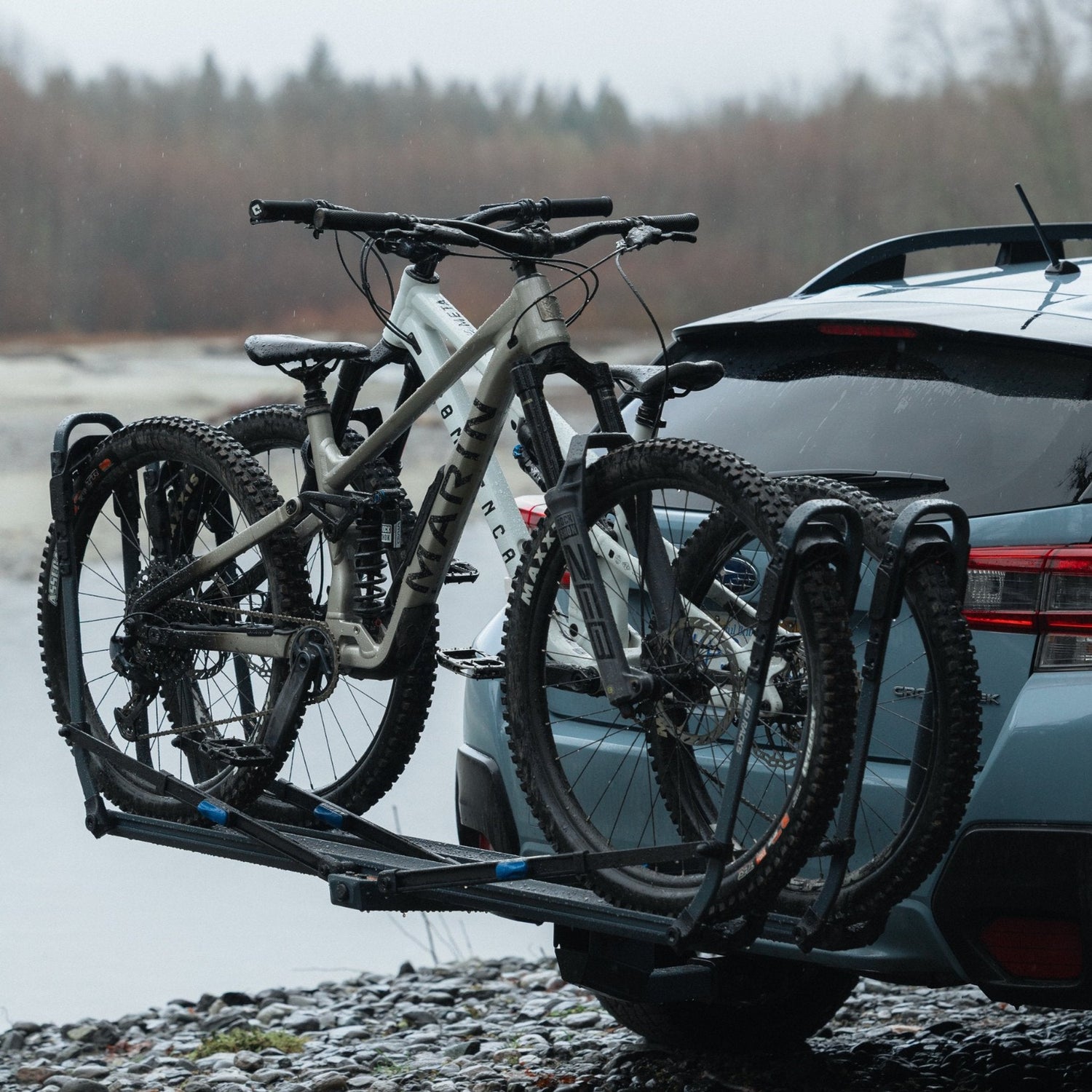 Bicycle rack attached to a car with two bicycles on a gravel road.
