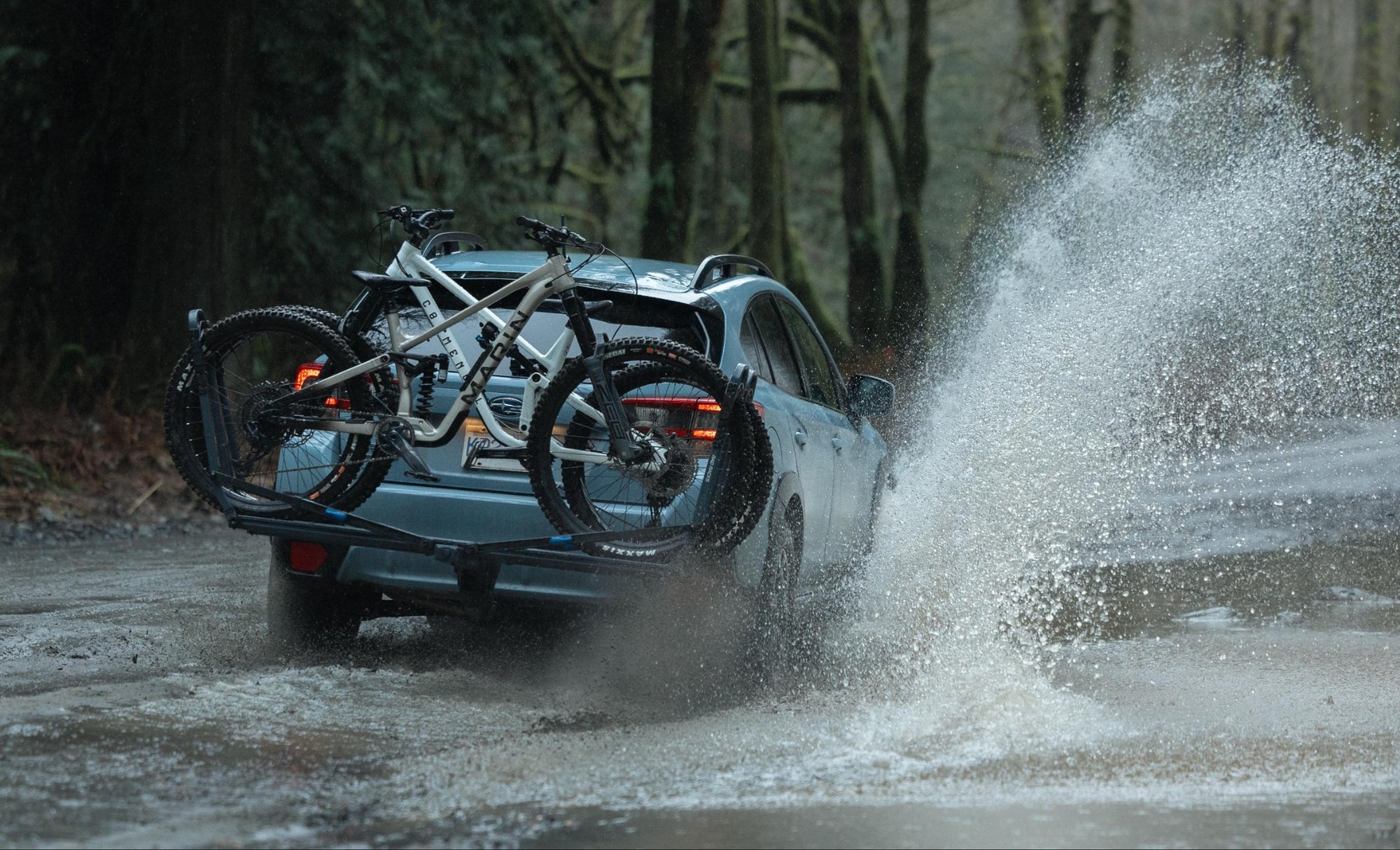 Car with bicycles on a roof rack driving through a muddy forest road.