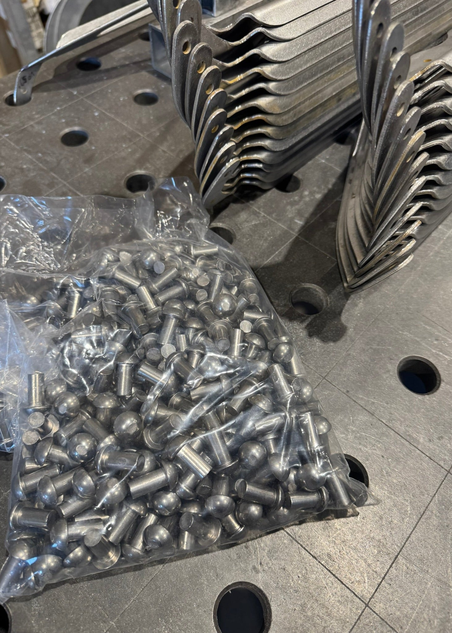 Metal components on a workbench with a bag of smaller metal parts.