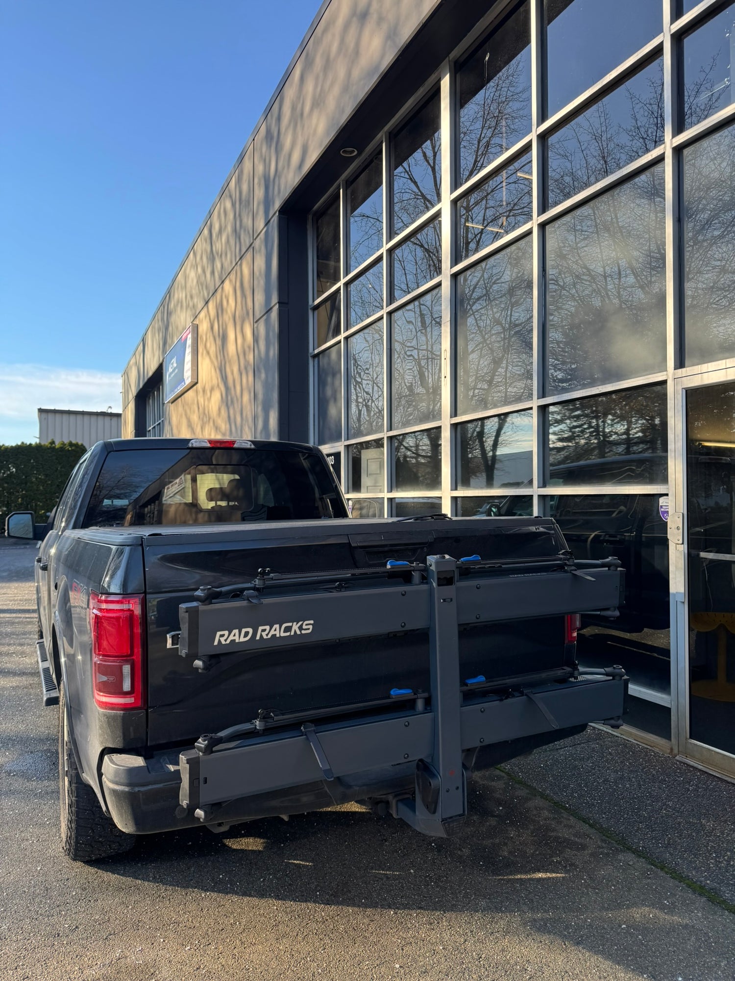 Black pickup truck with 'RAD RACKS' on a building with large windows. E bike rack tray bike rack easy loading ramp 