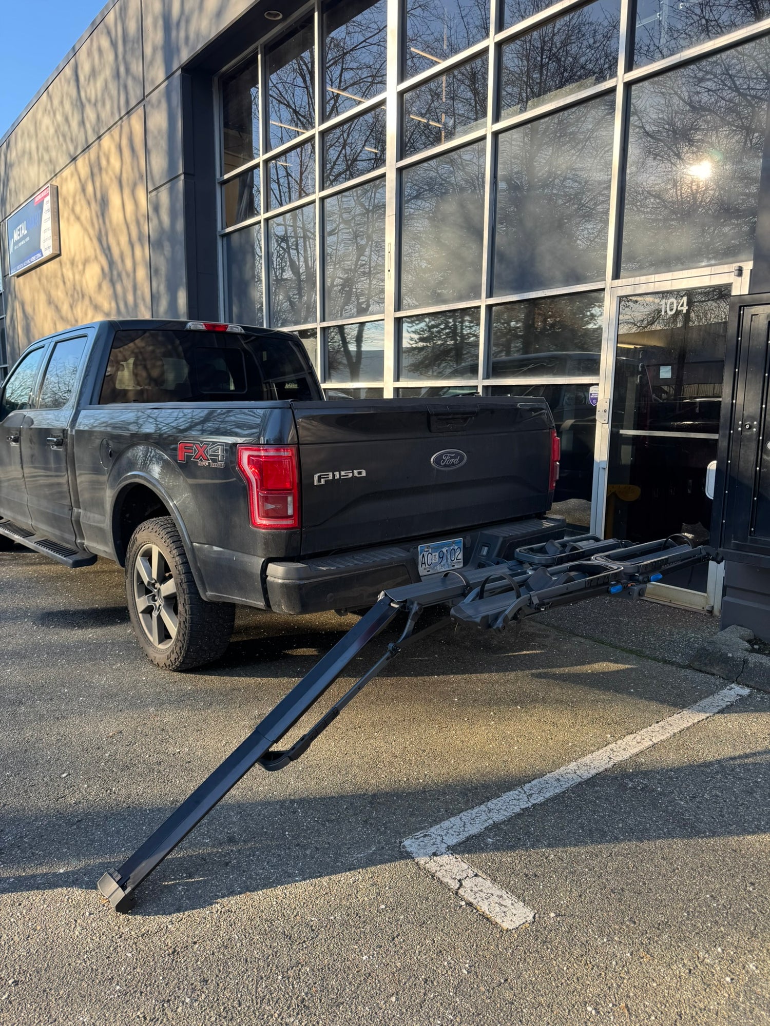 Black Ford truck with a trailer hitch in front of a building with large windows. Built in ramp loading Ebike e bike e-bike on tray bike rack Rad Racks