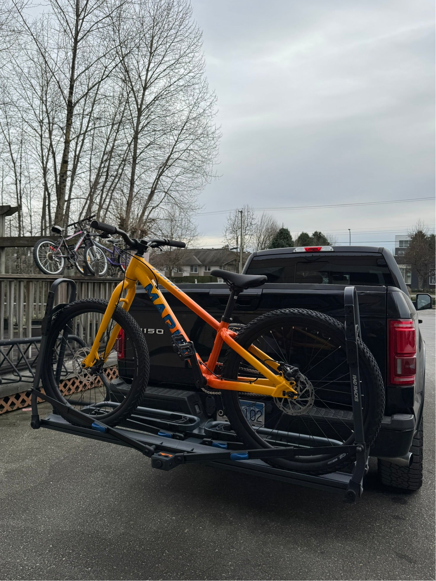 24" kids bike yellow bicycle on a bike rack attached to the back of a black pickup truck with a cloudy sky in the background.
