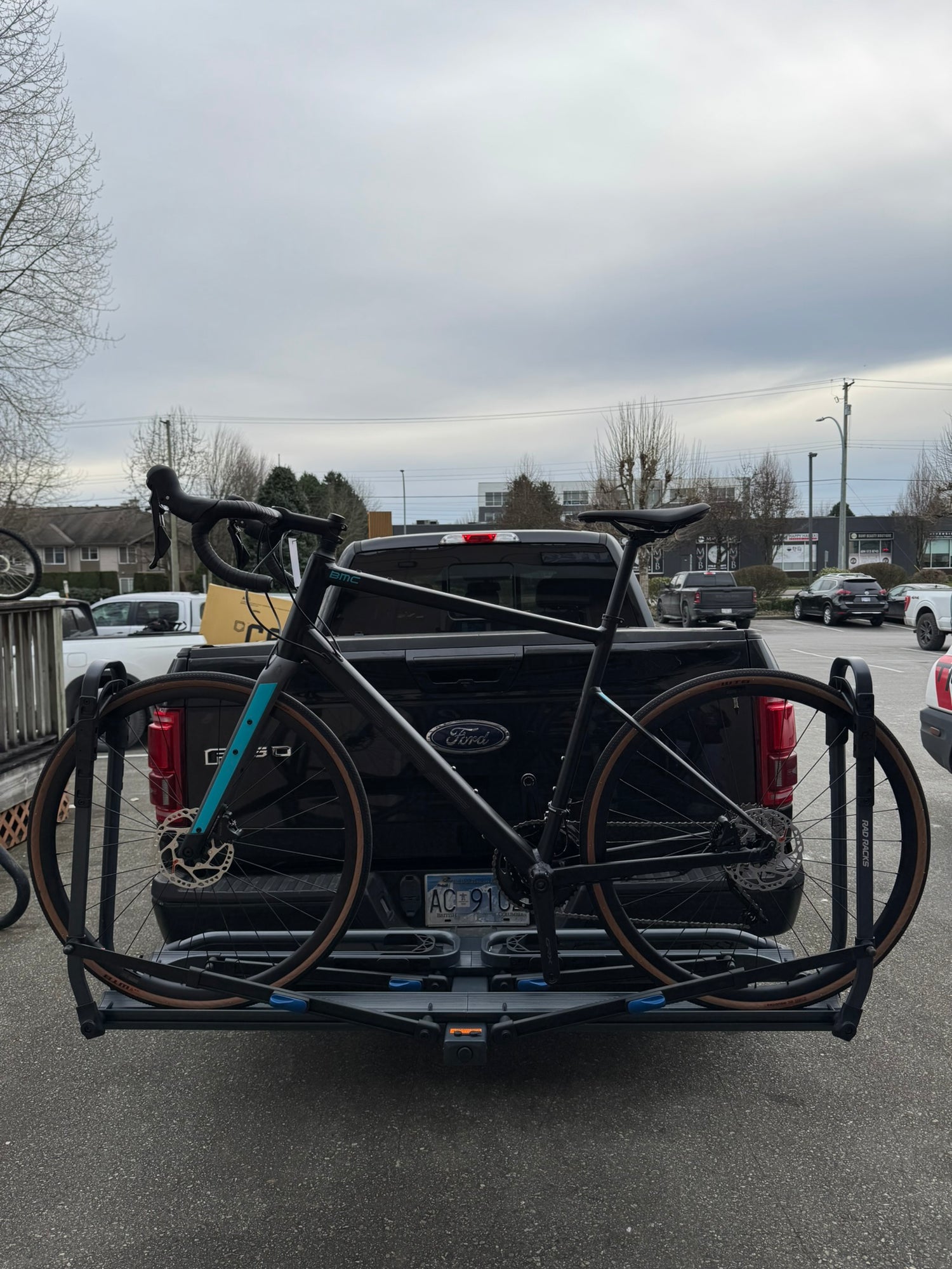 Gravel  Bicycle attached to a bike rack on the back of a black Ford truck in a parking lot.