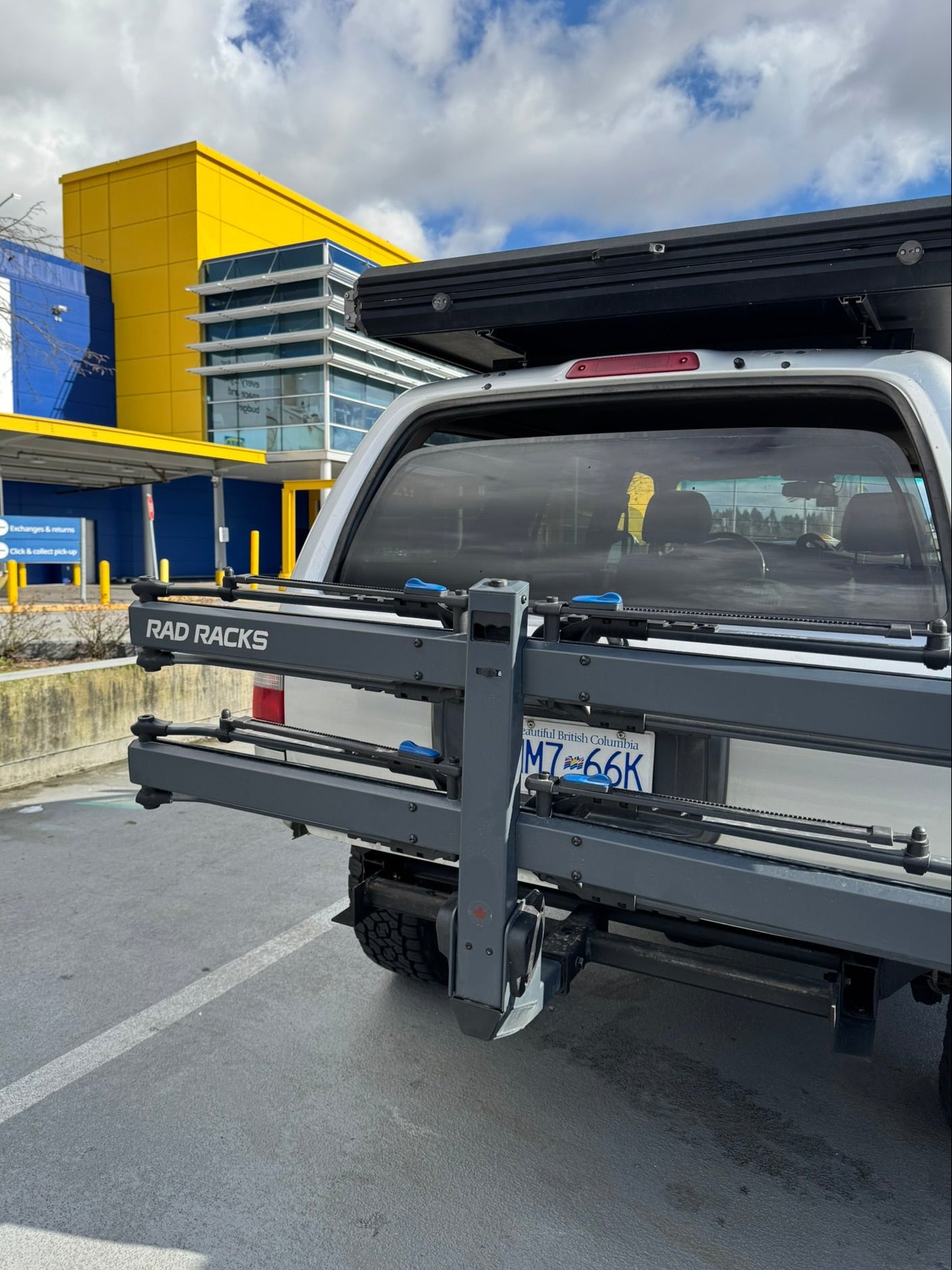 Truck with a RAD RACKS hitch receiver attached, parked in a lot with a building in the background. TRAY BIKE RACK