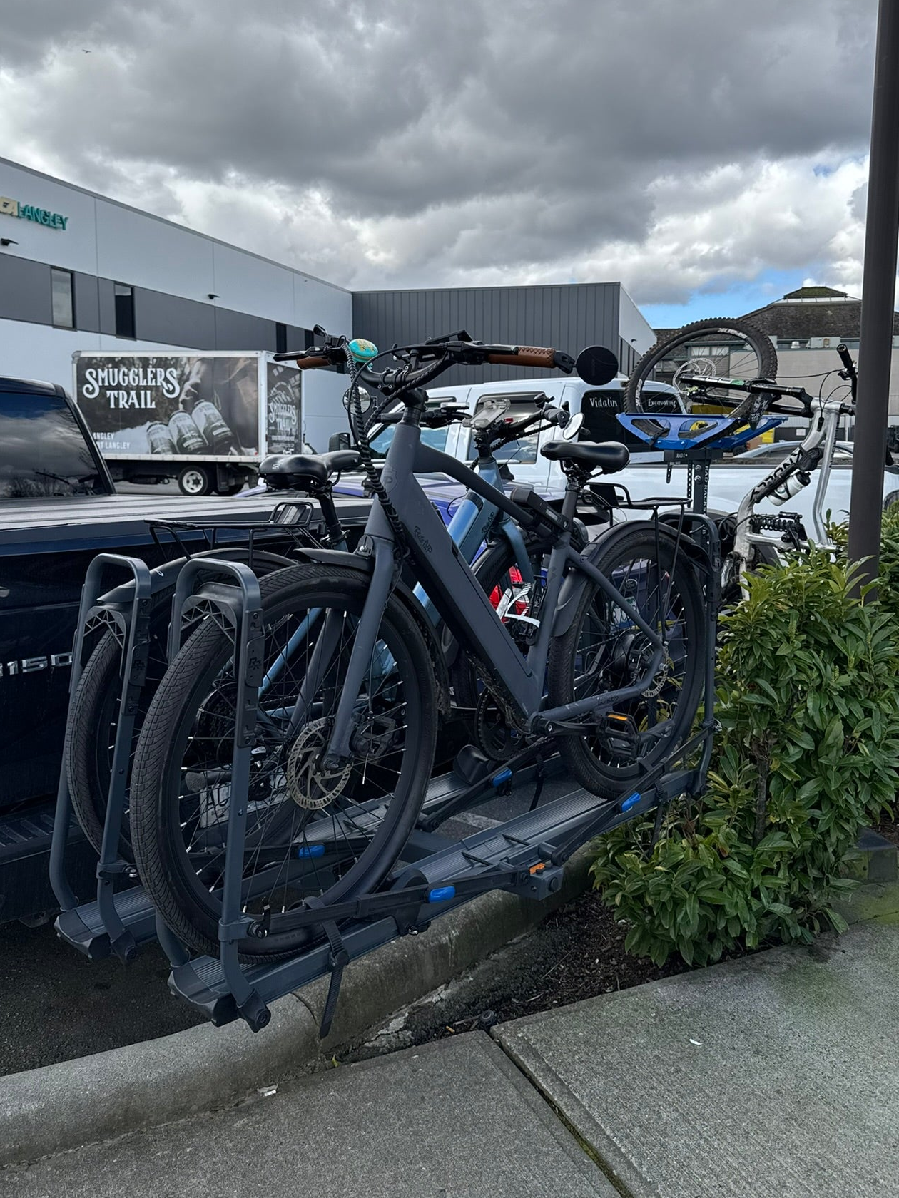 Bicycle rack attached to a truck with cloudy sky and buildings in the background. Ebike e bike e-bike on tray bike rack Rad Racks