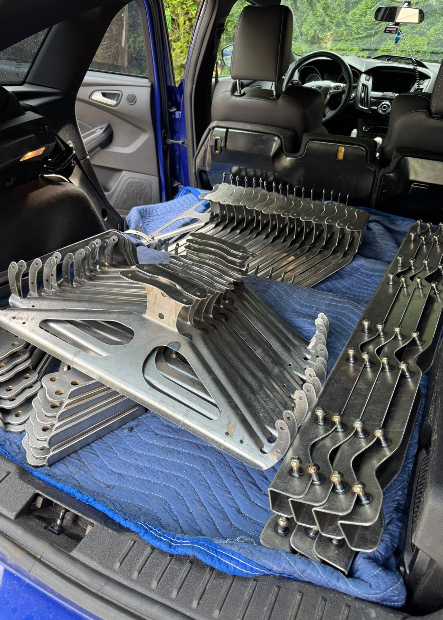 Metal brackets arranged on a blue towel inside a vehicle's open trunk.