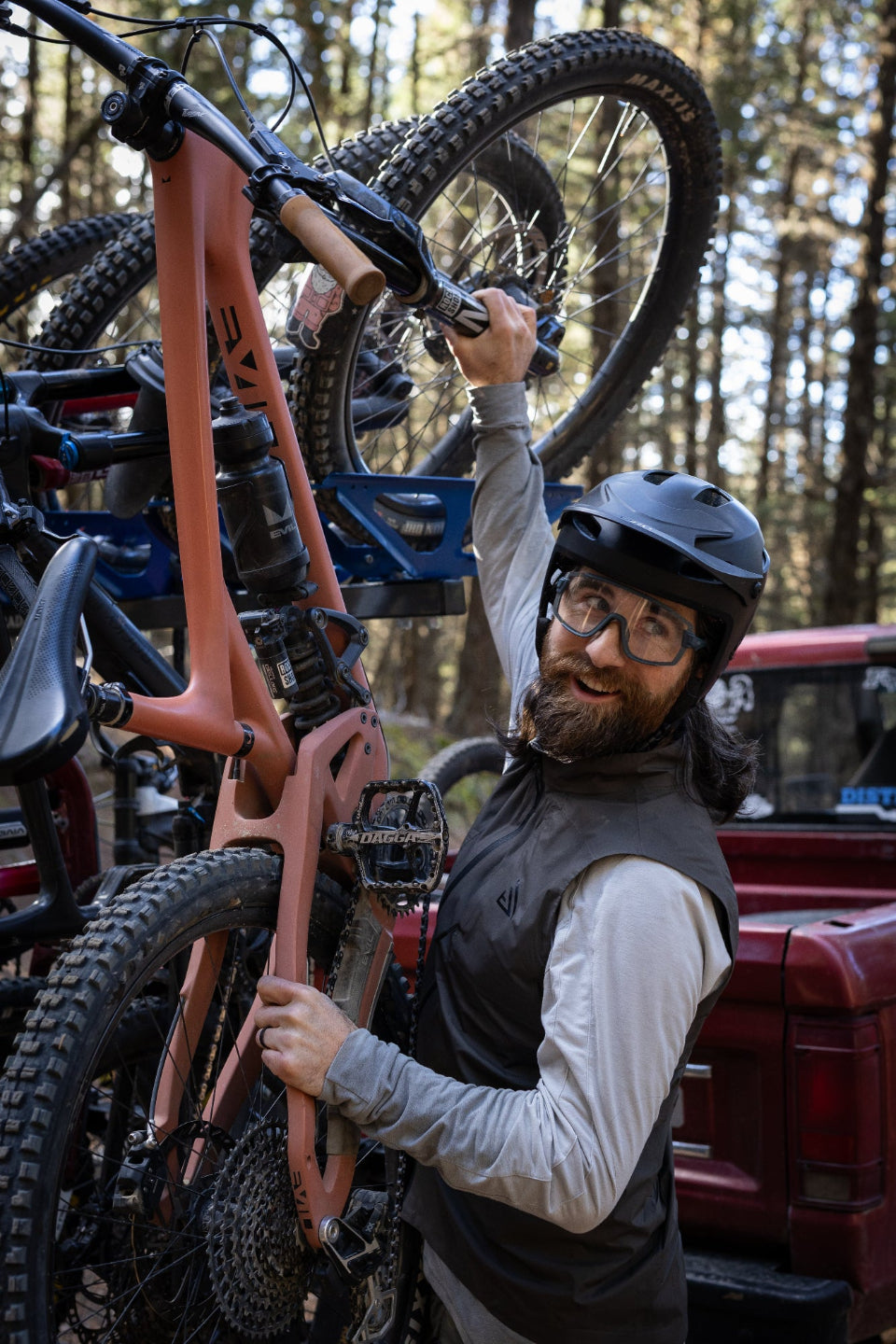 Man with a beard and helmet loading a bicycle onto a truck in a forest setting bike rack vertical
