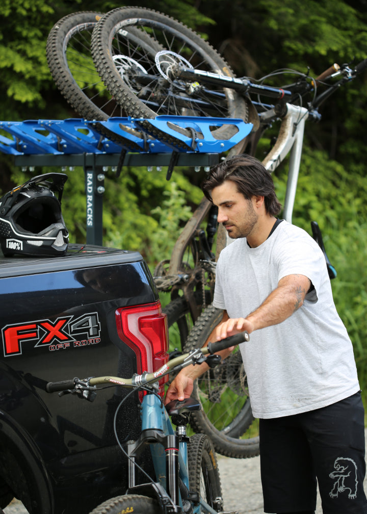 Man attaching a bike to a truck with a bike rack on a forested background